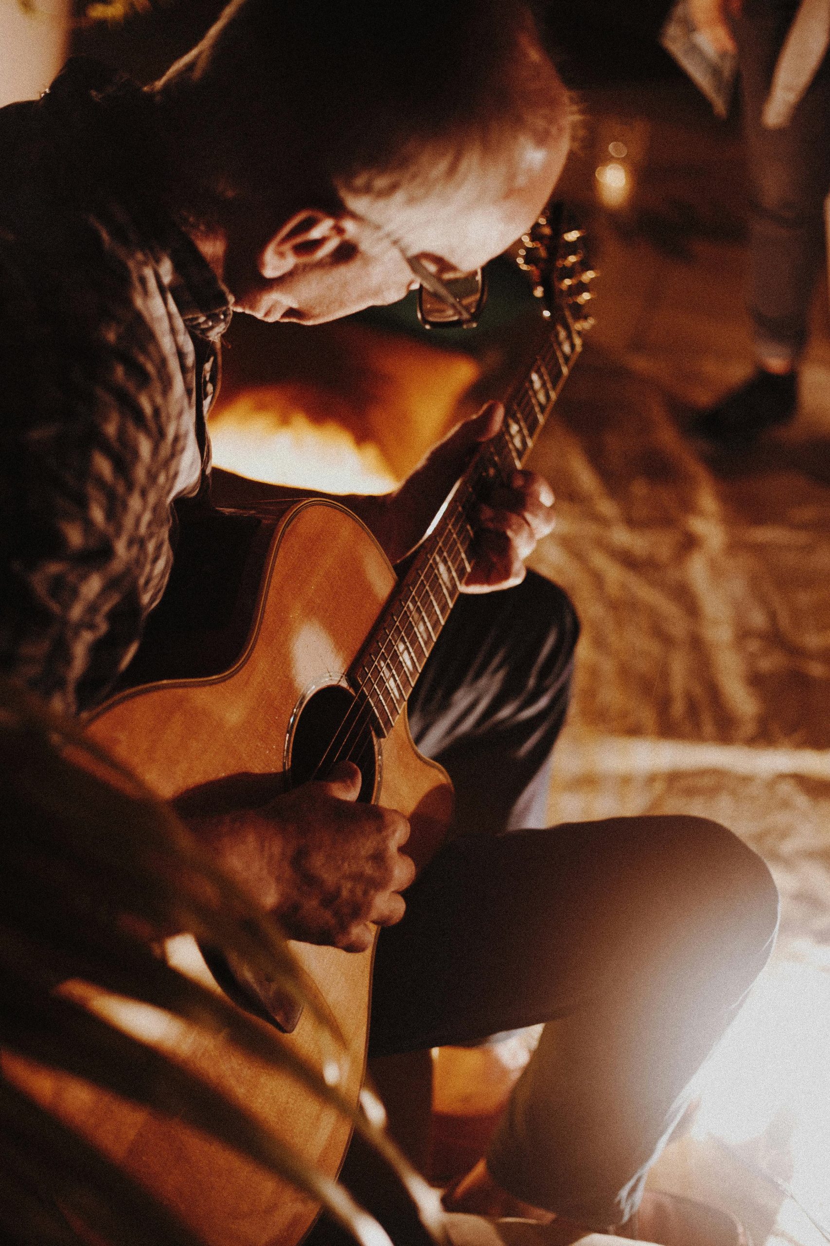 Man playing acoustic guitar by firelight creating a cozy atmosphere.